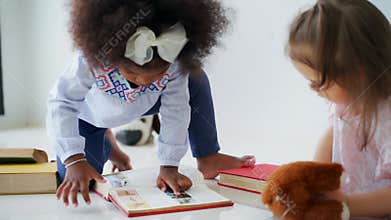 Cute little girls in casual clothing reading books and playing together in the room