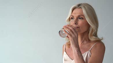 Smiling healthy thirsty fit mid aged 50s woman holding glass drinking water.