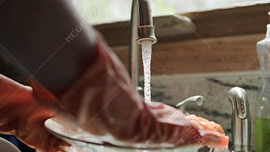 hands in orange gloves wash dishes in the kitchen. Close up