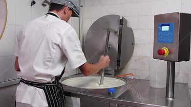 A man working at cheese production factory - adding a thickener into a vat with a cheese base