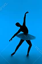Beautiful silhouette of ballerina on blue background dancing ballet. Woman performs smooth movements. Sensual dancer in
