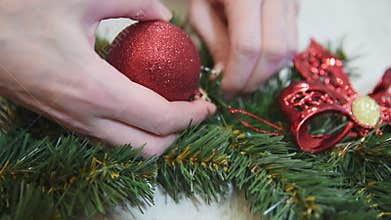Close up female hands decorate a Christmas wreath with red shiny ball. Making crafts. Seasonal holiday workshop online