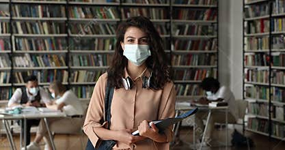 Attractive student girl wear protective face mask posing in library
