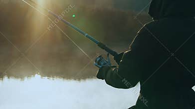 rays of the rising sun light on man fishing at the riverbank