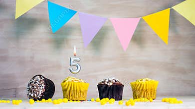 Birthday background with number 5. Beautiful birthday card with colorful garlands, a muffin with a candle burning copyspace.