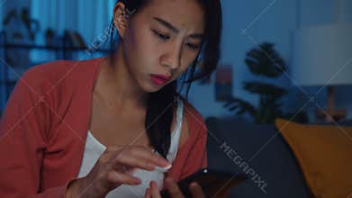 Night time upset Asia lady use smartphone sitting on sofa in living room feel serious and stress with bad news or message in