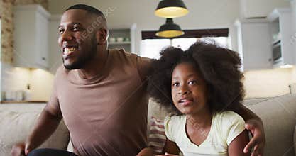 African american daughter and her father on couch watching tv eating popcorn and cheering