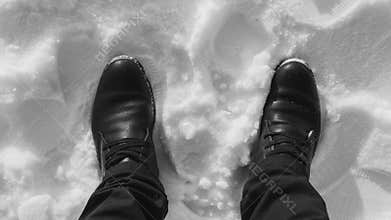 Boots in the snow, a man stands in a snow-white black-and-white photo, top view with his feet in the snow.