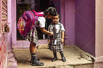 A girl helps her little sister with her school uniform.