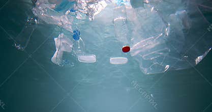 Plastic waste contaminating the ocean. Cinematic under water view of packaging garbage float in light rays slow motion.