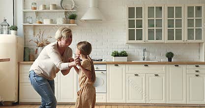 Little girl dancing with elderly grandmother in kitchen