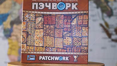 Patchwork board game against a blurry world map. The camera flies around. Parallax effect. Inscription in Russian: Uwe Rosenberg`s