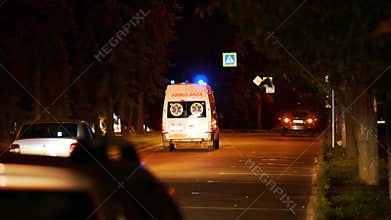 An ambulance with flashing beacons on rushes along a city street at night.