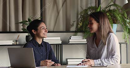 Indian and Caucasian colleagues talking seated at desk in office