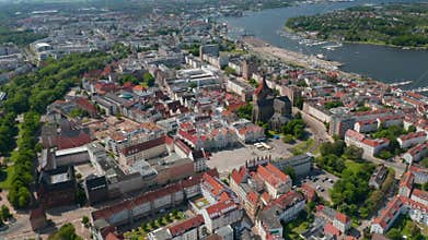 Forwards fly above town. Aerial view of city at river or sea bay. Tilt down footage of Neuer Markt square with gabled