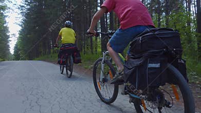 Two young men with backpacks ride bicycles along the road.