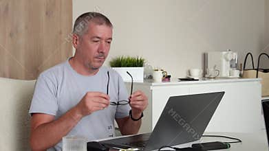A man working on a laptop puts on glasses to see better