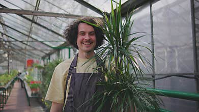 Male worker in a greenhouse. Portrait of a man holding a pot of beautiful green plants. Botanist salesman in a plant