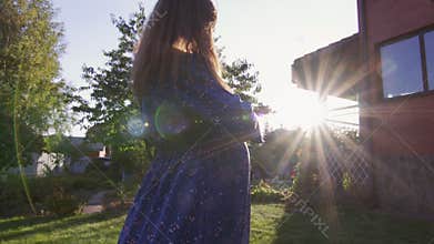 Beautiful pregnant woman enjoying fresh air at sunset rays on the backyard