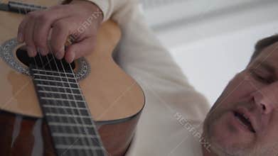 A man is playing an acoustic guitar with his eyes closed