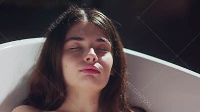 A woman is relaxing in a bathtub with a candle glowing in the background