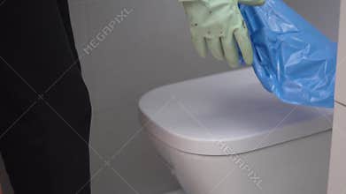 The cleaning lady puts on rubber gloves and opens a garbage plastic bag