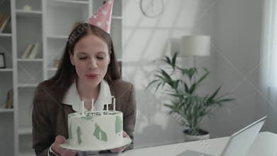 Charming Lady Office Worker Blowing Out Candles on Birthday Cake with Co-workers via Video Call.