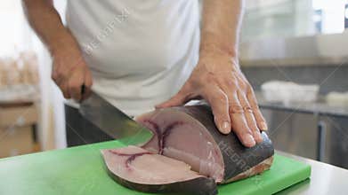 Knife Blade Cuts Slice Of Swordfish On A Chopping Board In A Restaurant Kitchen