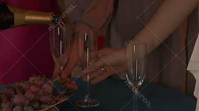Group of young women friends celebrating bachelorette party at home, close up shot of the table, bride pouring champagne