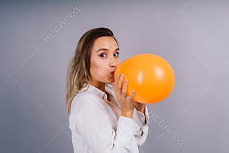 Close up portrait of a young woman inflating balloon on isolated grey background