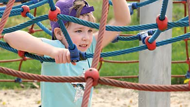 Young elementary school age girl wearing a baseball cap playing on the playground, climbing, portrait, face closeup, slow motion