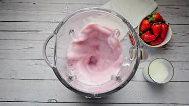 Fresh strawberry and milk into blender cooking milkshake, smoothie. Slow motion. Top view