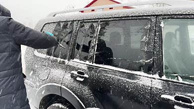 Man driver removing snow from auto glass window, using brush