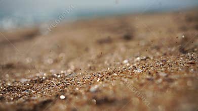 Sand flows in slow motion against the bokeh background of the beach and sea.