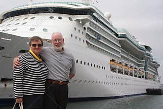 Happy Senior Couple Posing In Front of A Large DockedPassenger Cruise Ship.