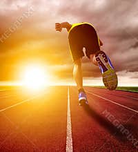 Athletic young man running on race track with sunset background