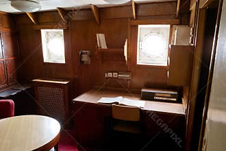 Vintage ship cabin interior featuring round windows and wooden furniture during daylight hours