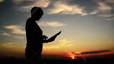 Woman using digital tablet computer for internet browsing. Female silhouette with modern gadget standing in sunset