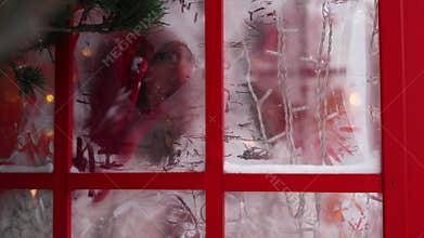 A Christmas concept, Happy woman in a fur coat posing in a red telephone booth on snowing day.