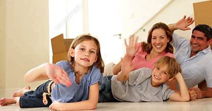 Happy family lying on floor in their new home waving at camera