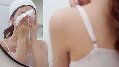 Beautiful young asian woman gently clean on face while looking mirror in bathroom, woman looking mirror with freshness while
