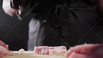 The chef turns over a pork chop and quickly beats a meat hammer on a wooden board.