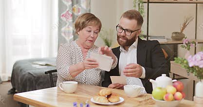 Good looking granny and adult grandson sitting and watching old photos. Mature woman and young man recalling old times