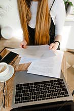Smart girl sitting with a laptop in cafe and examines the paper in her hands,reads text.Girl student studying at the table in a