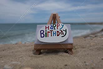 Happy Birthday text composed on stone over a canvas on the beach