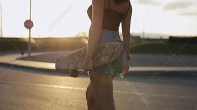 Woman skateboarder carries her skateboard in hands at sunset