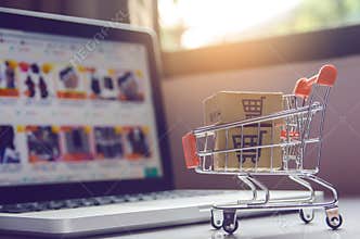 Shopping online concept - Parcel or Paper cartons with a shopping cart logo in a trolley on a laptop keyboard. Shopping service on