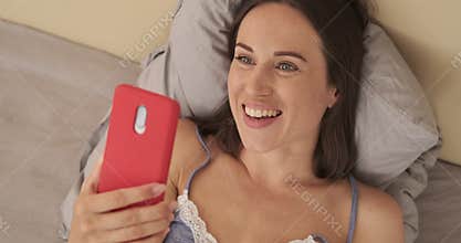 Woman laughing while doing video chat using mobile phone in bed
