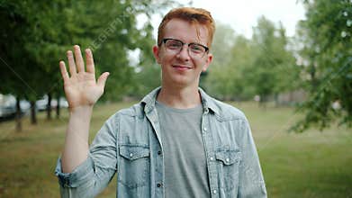 Portrait of attractive guy waving hand greeting people and smiling in green park