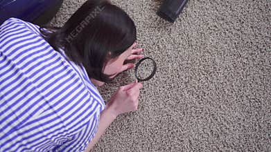 Young woman examines the carpet with a magnifying glass,view from the top